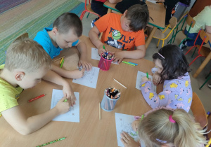 Kilkoro dzieci przy stole koloruje symbole pokoju.