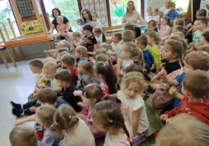 Młodsze dzieci siedzą na dywanie podczas audycji muzycznej.