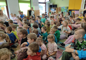 Starsze dzieci siedzą na dywanie podczas audycji muzycznej.