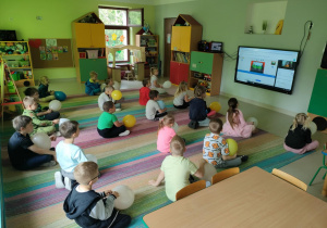 Dzieci siedzą na dywanie i uważnie oglądają, na czym polega wizualny język programowania Scratch Junior.