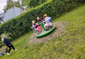 Dzieci w trakcie zabawy na karuzeli w ogrodzie przedszkolnym.