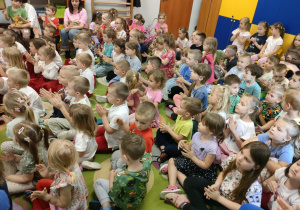 Przedszkolaki siedzą na dywanie i klaszczą do rytmu, przy akompaniamencie gitary elektrycznej.