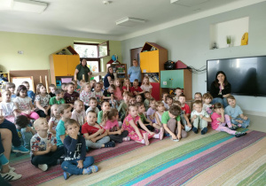 Starsze dzieci siedzą na dywanie i uważnie słuchają przybyłych Gości.