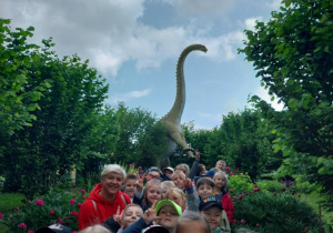 "Biedroneczki" wraz z nauczycielką na tle ogromnego dinozaura.