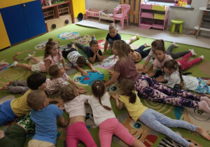 Pani Kasia prezentuje dzieciom młodszym podstawową pozycję podczas ćwiczeń jogi.