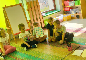 Grupa dzieci omawia złożoną przez siebie planszę edukacyjną.