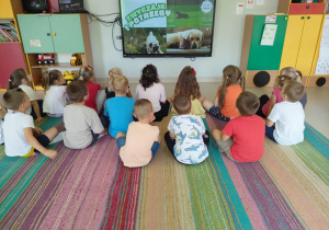 Dzieci oglądają film edukacyjny pt. "Kodeks przyjaźni z psem" na ekranie multimedialnym.