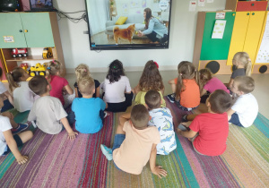 Dzieci oglądają film edukacyjny pt. "Kodeks przyjaźni z psem" na ekranie multimedialnym.