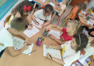 "Pszczółki" siedzą przy stoliku i rozwiązują zadania związane z programem "Psia Lekcja".