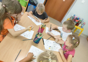 "Pszczółki" siedzą przy stoliku i rozwiązują zadania związane z programem "Psia Lekcja".
