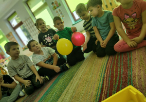 Dzieci siedzą na dywanie i porównują balony.