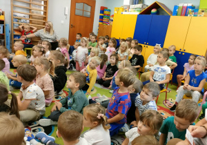 Przedszkolaki siedzą i słuchają nowej piosenki na powitanie.