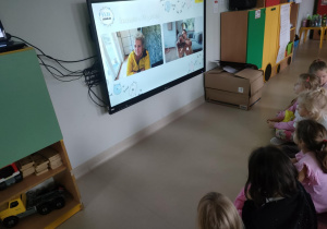 Dzieci oglądają sztuczkę w wykonaniu pieska na ekranie multimedialnym.