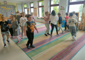 Dzieci podczas matematycznych potyczek ruchowych, polegających na przeliczaniu i wykonywaniu ćwiczenia związanego z danym wynikiem. Plansze przczepione zostały nad ekranem multimedialnym.