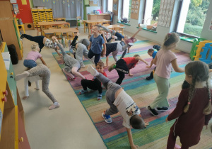 Dzieci podczas matematycznych potyczek ruchowych, polegających na przeliczaniu i wykonywaniu ćwiczenia związanego z danym wynikiem. Plansze przczepione zostały nad ekranem multimedialnym.