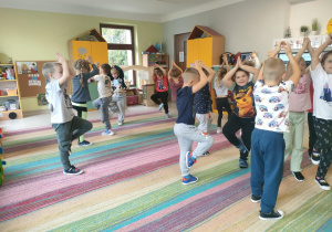 Dzieci podczas matematycznych potyczek ruchowych, polegających na przeliczaniu i wykonywaniu ćwiczenia związanego z danym wynikiem. Plansze przczepione zostały nad ekranem multimedialnym.