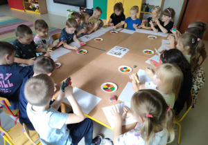 Dzieci siedza przy połączonych stołach i malują swoje dłonie, przy wykorzystaniu farb w jesiennych kolorach i gąbeczek.