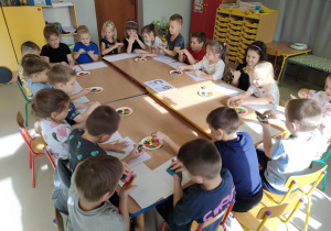Dzieci siedza przy połączonych stołach i malują swoje dłonie, przy wykorzystaniu farb w jesiennych kolorach i gąbeczek.