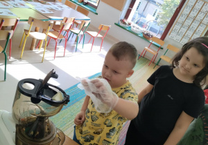Dzieci kolejno, w rękawiczkach wrzucają kawałki jabłka/marchewki do wyciskarki wolnobrotowej.