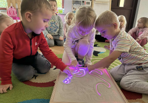 Dzieci tworzą obrazy z piasku na podświetlanym panelu.