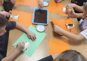Dzieci za pomocą pędzelków, nakładają klej na kubeczek, przyczepiony do kolorowej kartki.