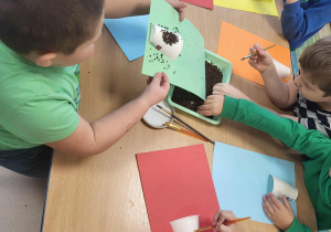 Dzieci za pomocą pędzelków, nakładają klej na kubeczek, przyczepiony do kolorowej kartki.