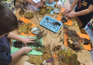 Przedszkolaki przy stołach tworzą swoje bukiety z jesiennych liści.