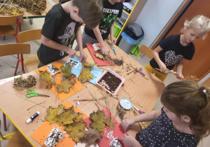 Przedszkolaki przy stołach tworzą swoje bukiety z jesiennych liści.