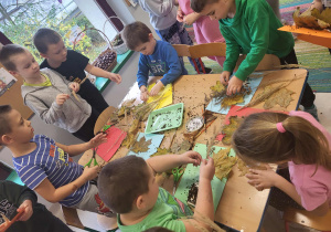 Przedszkolaki przy stołach tworzą swoje bukiety z jesiennych liści.