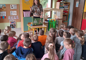 Nauczycielka Justyna Tomczak zaprasza dzieci do oglądania teatrzyku kamishibai pt. "Jesienny bal w lesie".