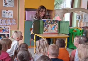 Wychowawczyni grupy Pszczółek czyta dzieciom treść scenki "Jesienny bal w lesie".