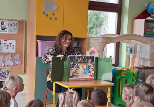 Pani Justyna Tomczak czyta dzieciom treść bajki "Jesienny bal w lesie" z wykorzystaniem teatrzyku kamishibai.