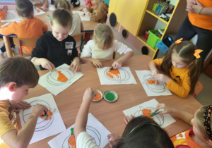 "Pszczółki" malują szablon dyni za pomocą gąbki i farby.