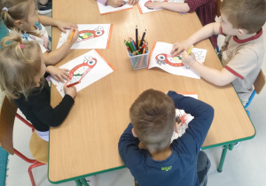 Kilkoro dzieci przy stoliczku koloruje szablon papugi zgodnie z podanymi kolorami.