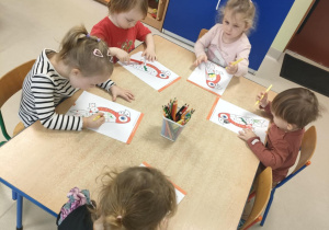 Kilkoro dzieci przy stoliczku koloruje szablon papugi zgodnie z podanymi kolorami.