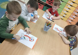 Kilkoro dzieci przy stoliczku koloruje szablon papugi zgodnie z podanymi kolorami.