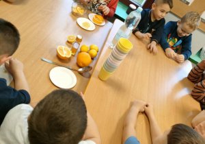 Chłopcy po kolei układają plasterki pomarańczy i cytryny w dzbanku.