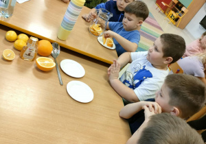 Chłopcy po kolei układają plasterki pomarańczy i cytryny w dzbanku.