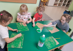 Dzieci malują tekturę na zielono.