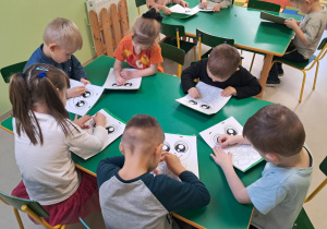 Dzieci nakłuwają szablon żabki.