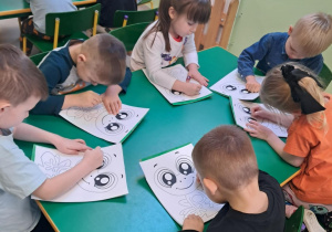 Dzieci nakłuwają szablon żabki.