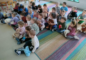 Połączone grupy maluszków i starszaków oglądają film edukacyjny o Dniu Pluszowego Misia na ekranie multimedialnym.