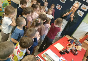 Przedszkolaki oglądają wystawę elementów kultury japońskiej, podczas gdy p. Dariusz omawia poszczególne przedmioty.