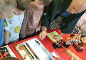 Przedszkolaki oglądają wystawę elementów kultury japońskiej, podczas gdy p. Dariusz omawia poszczególne przedmioty.