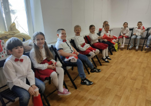 Dzieci siedzą na krzesełkach i oczekują na swój występ.