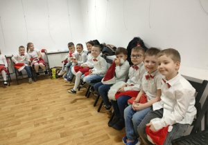 Dzieci siedzą na krzesełkach i oczekują na swój występ.