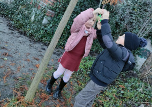 Dzieci razem przyczepiają woreczek z pokarmem dla ptaków na zimę.