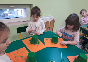 Kilkoro dzieci z grupy "Żabek" maluje zieloną farbą małą doniczkę.