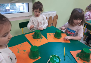 Kilkoro dzieci z grupy "Żabek" maluje zieloną farbą małą doniczkę.