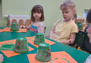 Kilkoro dzieci z grupy "Żabek" maluje zieloną farbą małą doniczkę.